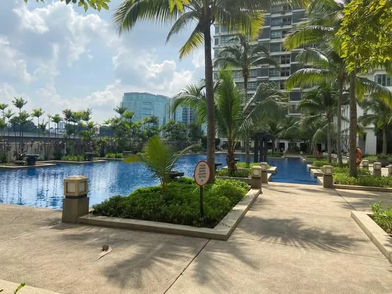 Exterior type: swimming pool deck; features: infinity pool, palm trees, manicured landscaping, concrete walkway, poolside loungers, surrounding greenery, modern high-rise buildings in background, sunny weather, signage near pool area; style: modern.