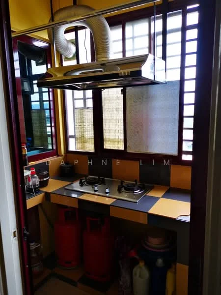 Kitchen features: black and yellow checkered countertop, 2-burner gas hob, stainless-steel range hood, red gas cylinder, wooden cabinetry, window with wooden slats, bamboo blinds, wall-mounted ventilation duct, shelves for storage, bottles on countertop; style: modern.