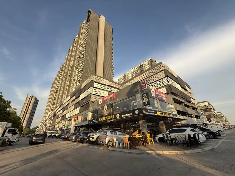 Exterior type: mixed-use development; features: high-rise building with multiple floors, glass curtain wall facade, commercial units at ground level, outdoor seating area, parking spaces visible, surrounding vehicles, urban context with nearby buildings, clear blue sky; style: modern.