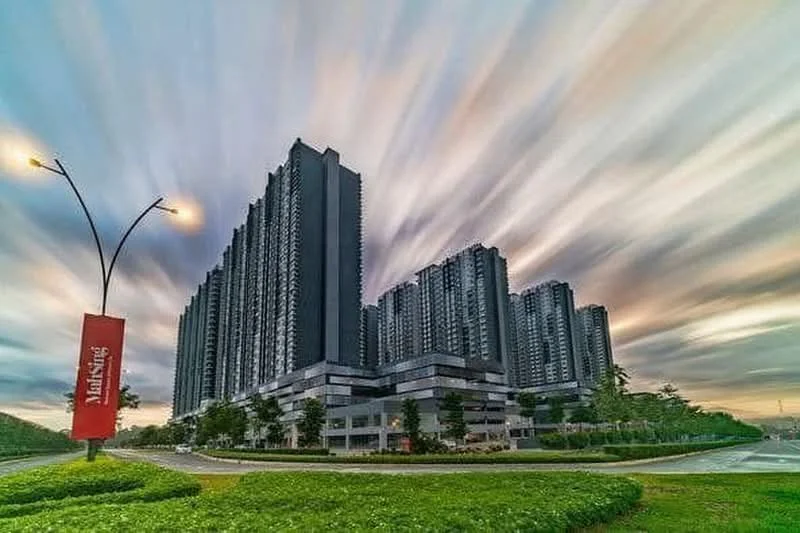 Exterior type: high-rise condominium; features: glass curtain wall, dark grey facade, multiple storeys, landscaped greenery in foreground, street lighting, signage at entrance, surrounded by open space; style: modern.