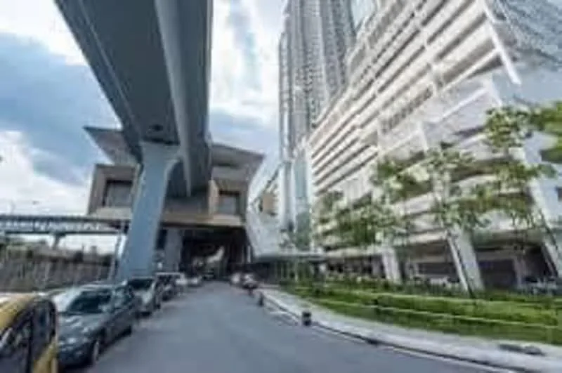 Exterior type: high-rise condominium; features: glass curtain wall, exposed concrete facade, projecting balconies, manicured lawn, surrounded by mature greenery, multi-storey car park, driveway with interlocking pavers; style: modern.