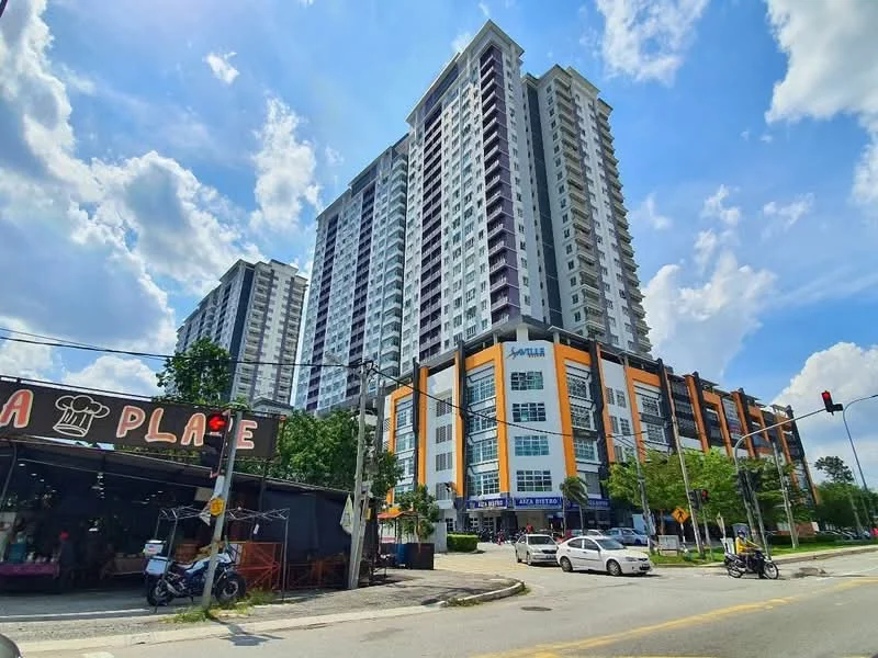 Exterior type: high-rise condominium; features: glass curtain wall, orange and grey painted facade, multiple storeys, balconies on upper floors, commercial units on ground level, surrounded by greenery, street view with traffic signals, parking spaces visible, urban context with nearby shops; style: modern.