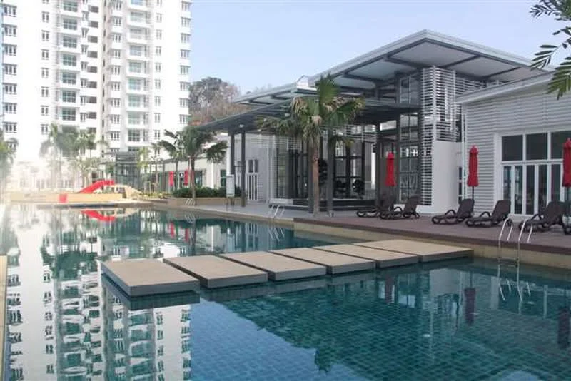 Exterior type: swimming pool deck; features: infinity pool, pool deck with loungers, red umbrellas, landscaped greenery, modern clubhouse, children's slide, glass facade, surrounded by high-rise buildings; style: modern.