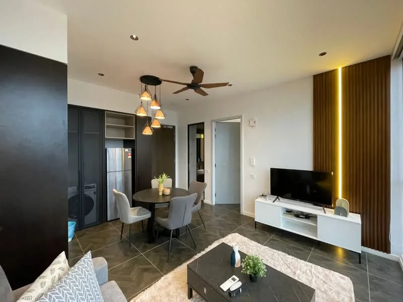 Living features: 5-blade ceiling fan with light, wall-mounted TV, white TV console, grey fabric sofa, round dining table, 4 upholstered dining chairs, pendant lighting with multiple bulbs, dark wood accent wall, light wood paneling, dark tiled flooring, decorative plant in vase, coffee table, refrigerator visible in background; style: modern.