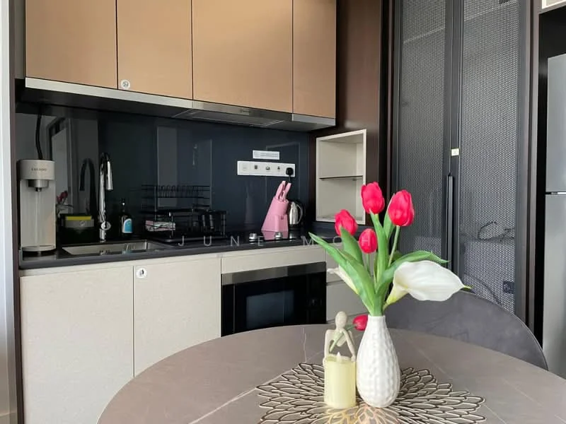 Kitchen features: light brown cabinetry, black countertop, stainless-steel sink, chrome pull-down faucet, built-in oven, stainless-steel fridge, black backsplash, kitchen island with seating, decorative vase with flowers, table with circular design, kitchen utensils on countertop, wall-mounted kitchen storage; style: modern.