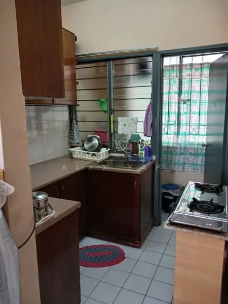 Kitchen features: brown wooden cabinetry, grey countertop, single-bowl stainless-steel sink, chrome pull-down faucet, 2-burner gas hob, white tiled backsplash, white tiled flooring, window with sheer curtains, refrigerator, kitchen rug, various kitchen utensils and containers.
