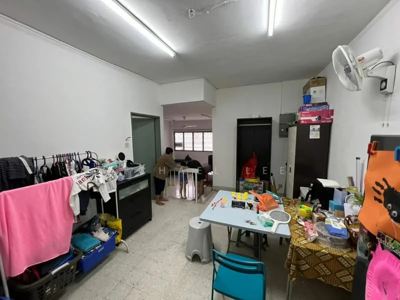 Room features: white painted walls, tile flooring, fluorescent ceiling lights, wall-mounted air conditioning unit, clothes drying rack, plastic storage bins, dining table with chairs, various household items on table, open space layout.