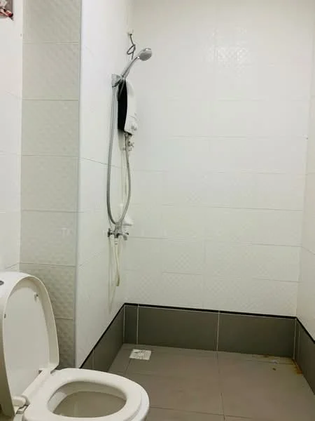 Bathroom features: white tiled walls, grey tiled flooring, toilet, shower with handheld showerhead, shower wall-mounted water heater.