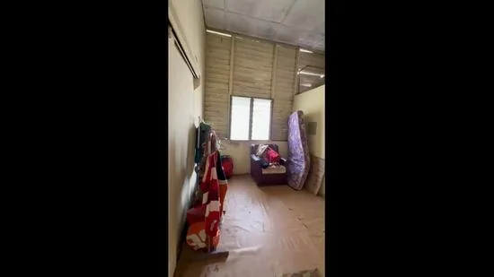 Room features: wooden flooring, plain walls, window with blinds, sofa, mattress, storage bags, cardboard boxes, exposed ceiling.