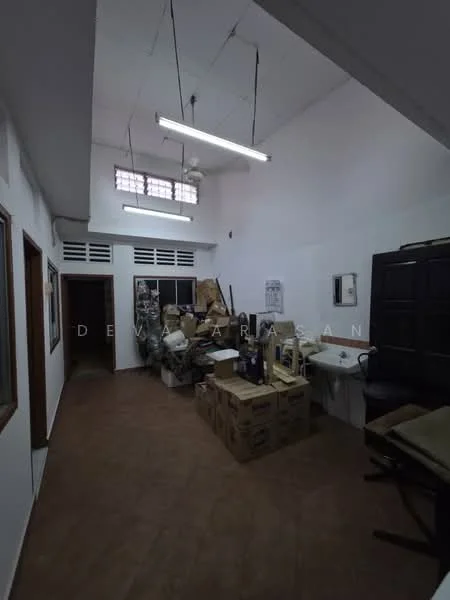 Room features: white painted walls, brown tiled flooring, exposed ceiling with fluorescent lights, window with grid pattern, sink, wooden cabinets, boxes and miscellaneous items, ceiling fan.