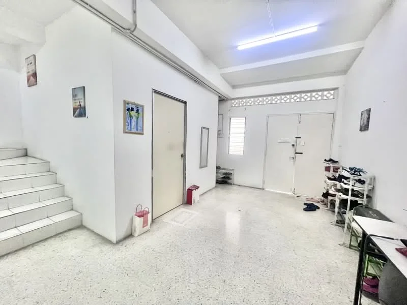 Room features: white painted walls, grey tiled flooring, staircase with white tiles, ceiling with fluorescent lighting, two doors, window with horizontal slats, shoe rack, small table, decorative wall art; style: minimalist.