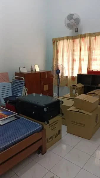 Room features: white painted walls, tiled flooring, ceiling fan, window with sheer curtains, wooden furniture, cardboard boxes, suitcases, bed with mattress, foldable chair.