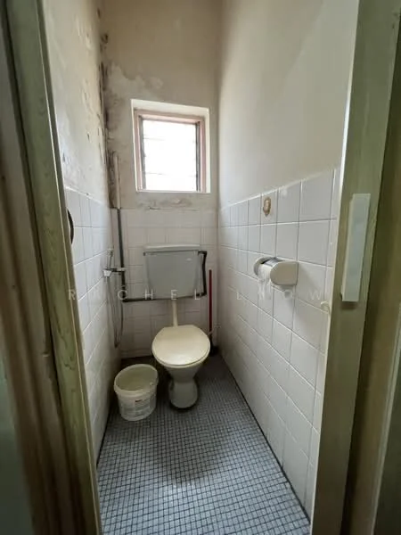 Bathroom features: white tiled walls, grey tiled flooring, one-piece toilet, toilet paper holder, small window, bucket, flush tank, wall-mounted mirror.