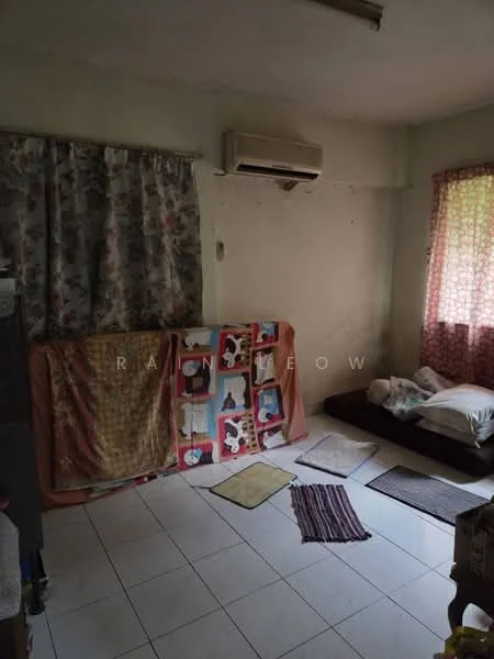 Room features: white tiled flooring, cream painted walls, window with floral curtain, wall-mounted air conditioning unit, bed with bedding, blankets draped over furniture, various small rugs on the floor, natural light from window.