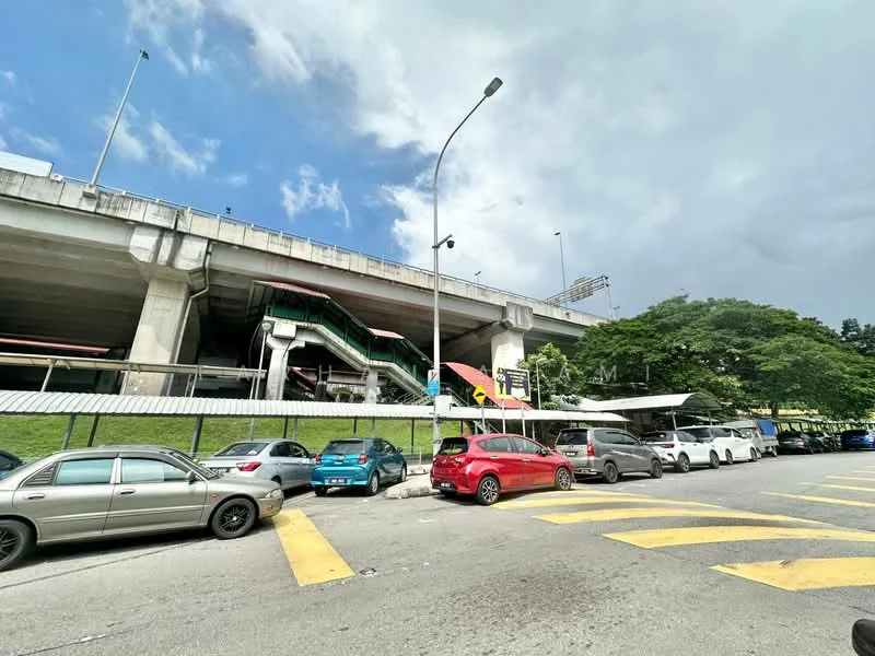 Exterior features: elevated train station, concrete structure, green grass area, multiple parked cars, road with yellow markings, overcast sky; style: modern.