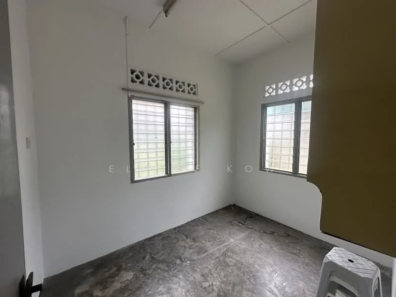Room features: concrete flooring, white painted walls, two windows with metal grilles, ceiling with light fixture, corner of room with yellow cabinetry, no visible furniture, neutral color scheme, natural light from windows; style: minimalist; view: garden.