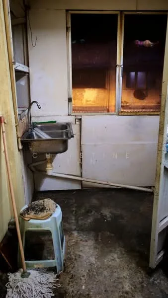 Laundry features: single-bowl stainless-steel sink, metal faucet, concrete flooring, white painted walls, window with metal frame, stool, mop, cleaning supplies, exposed plumbing, natural light from window.