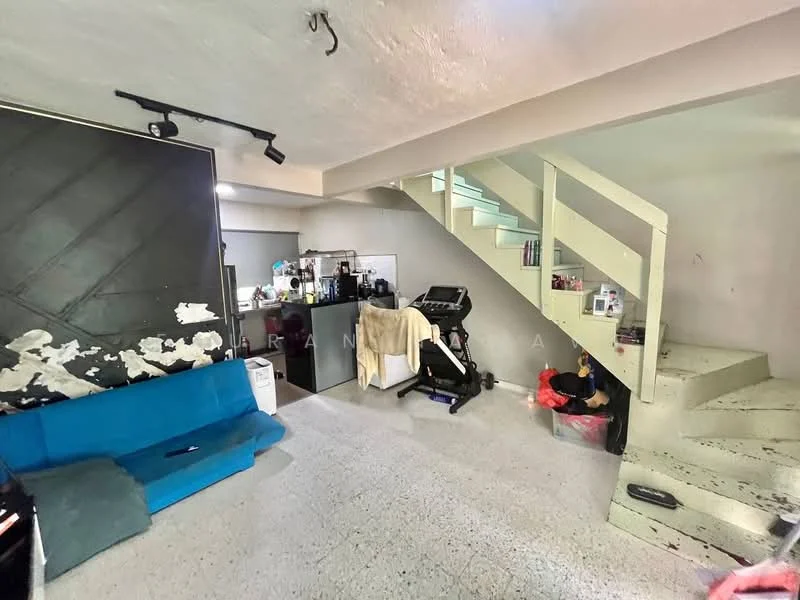Living features: blue fabric sofa, exposed concrete walls, grey flooring, staircase leading to upper level, recessed lighting, exercise equipment, open layout, kitchen area visible in background; style: modern.