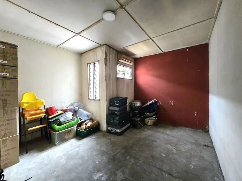 Room features: concrete flooring, white painted walls, grey accent wall, single window with metal grille, exposed ceiling, stacked boxes, plastic chairs, various storage containers.