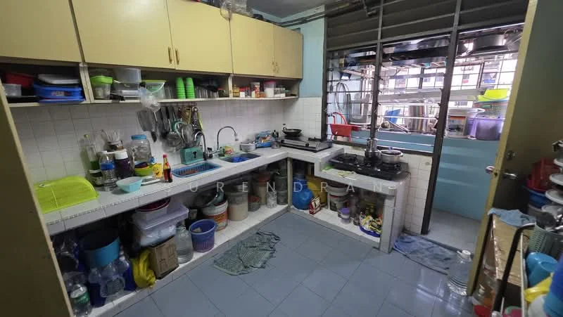 Kitchen features: light blue painted walls, white tiled backsplash, white laminate cabinetry, double-bowl stainless-steel sink, chrome pull-down faucet, freestanding gas stove, countertop with cluttered kitchenware, blue vinyl tile flooring, open shelving with various containers, window with metal grilles, multiple pots and pans visible, cleaning supplies on countertop.