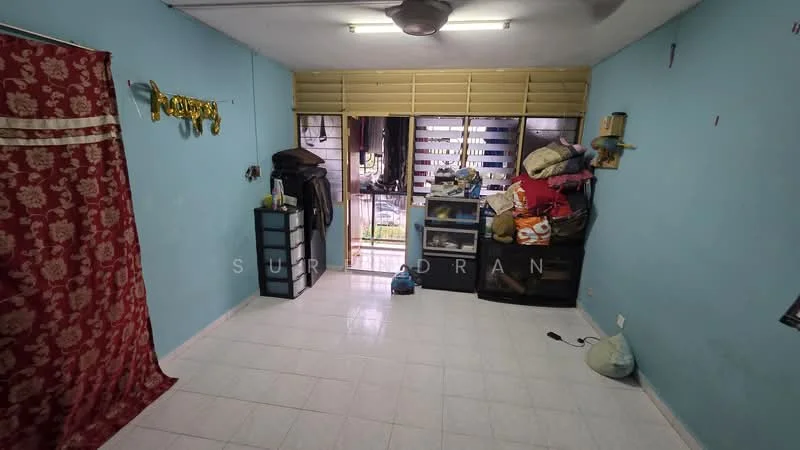 Room features: light blue painted walls, white tiled flooring, ceiling fan, large window with horizontal slats, curtains in red fabric, black storage cabinet, piled items on the floor, decorative wall letters, visible electrical outlet.