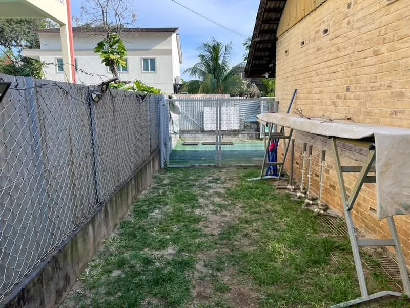 Exterior features: fenced yard with chain-link fence, grass lawn, concrete pathway, outdoor drying rack, paved area, surrounding trees, adjacent building visible, sunny outdoor space.