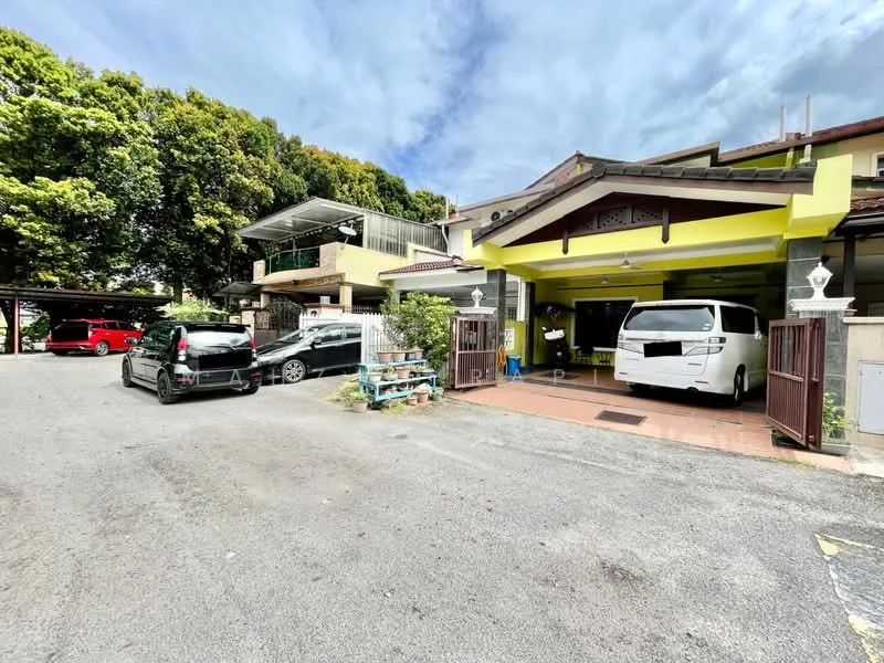 Exterior type: linked terrace house; features: car porch with awning, two vehicles parked in driveway, manicured landscaping, surrounded by mature trees, two-storey structure, yellow painted facade, covered parking area, brick pathway, front gate, open-air parking lot; style: modern.