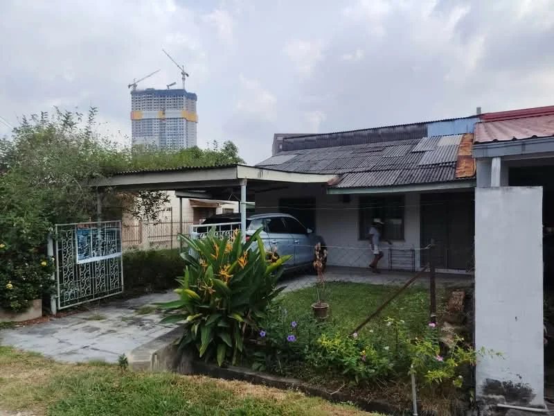 Exterior type: detached bungalow; features: single-storey, metal roofing, white painted facade, front garden with shrubs and flowers, paved walkway, car porch with awning, fenced yard, gate at entrance, surrounded by greenery, construction site visible in background; style: traditional.