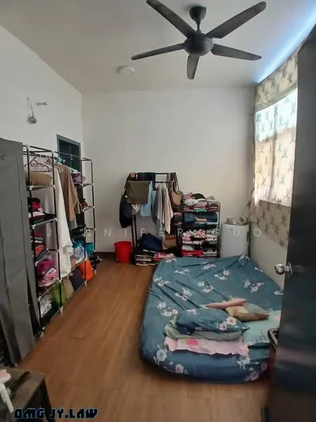 Bedroom features: wooden flooring, 5-blade ceiling fan, large window with sheer curtains, mattress on the floor, clothing racks, storage bins, folded clothes, decorative bedding with floral pattern.