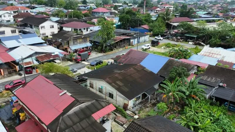 Exterior type: low-rise apartment block; features: flat roof, metal roofing, various roof colors including red and blue, surrounded by greenery, adjacent to a road, multiple residential units, visible parking spaces, tropical landscaping with palm trees, manicured lawns; style: traditional.