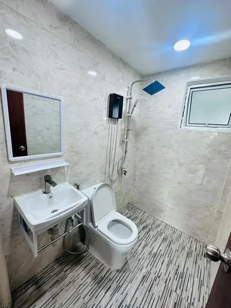 Bathroom features: white ceramic toilet, single-sink vanity with wall-mounted cabinet, chrome basin mixer faucet, framed mirror, walk-in shower with handheld showerhead, shower head on adjustable arm, tile cladding on walls, marble tile flooring, window for natural light, recessed ceiling lights; style: modern.