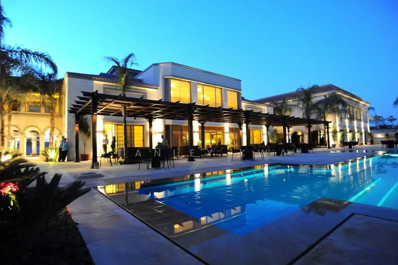 Exterior type: detached bungalow; features: swimming pool with loungers, outdoor dining area with pergola, landscaped garden with palm trees, manicured lawn, multiple storeys, large glass windows, modern facade with cream painted walls, stone-paved walkway; style: modern.