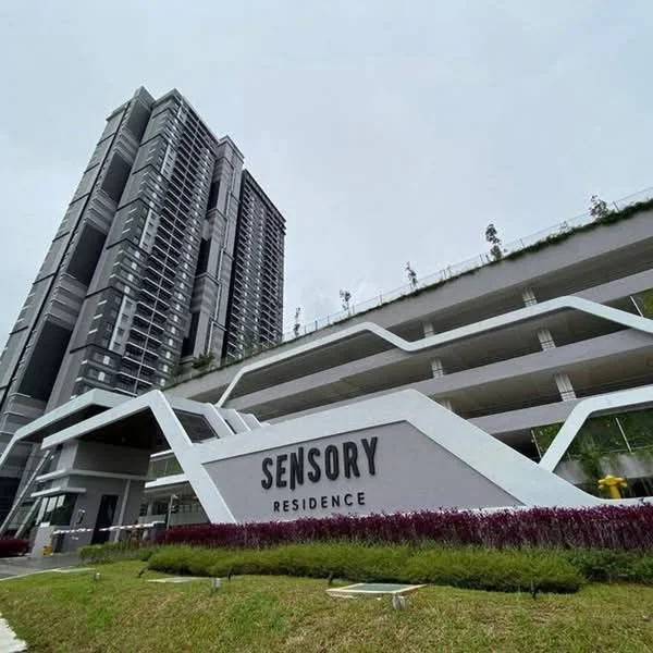 Exterior type: high-rise condominium; features: modern architectural design, grey concrete facade, large glass windows, recessed balconies, landscaped entrance with plants, signage with 'SENSORY RESIDENCE', multi-storey car park, manicured lawn, surrounded by greenery; style: modern.