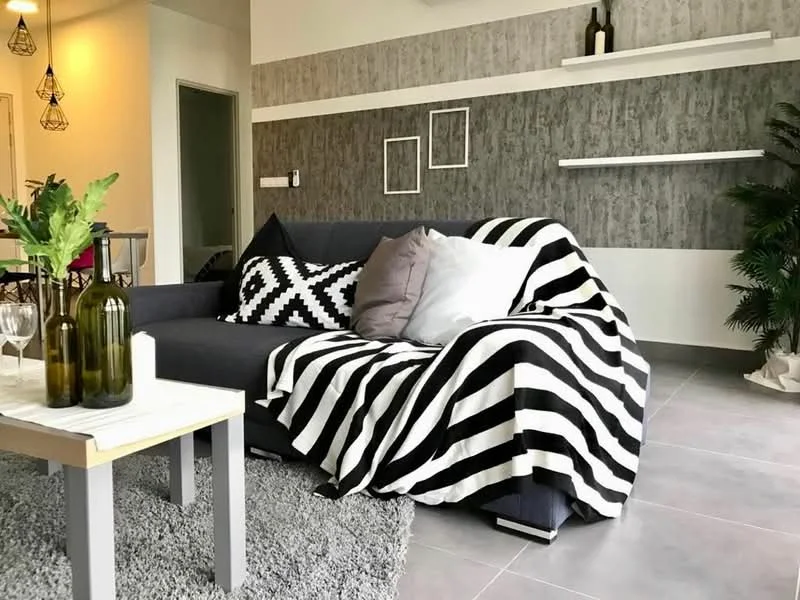 Living features: 3-seater fabric sofa in grey, black and white striped throw blanket, decorative cushions in various colors, area rug in light grey, wall-mounted shelves, grey accent wall with textured finish, white painted walls, indoor plant, coffee table with light wood finish, wine glasses, green glass bottles, pendant lighting fixtures; style: modern.