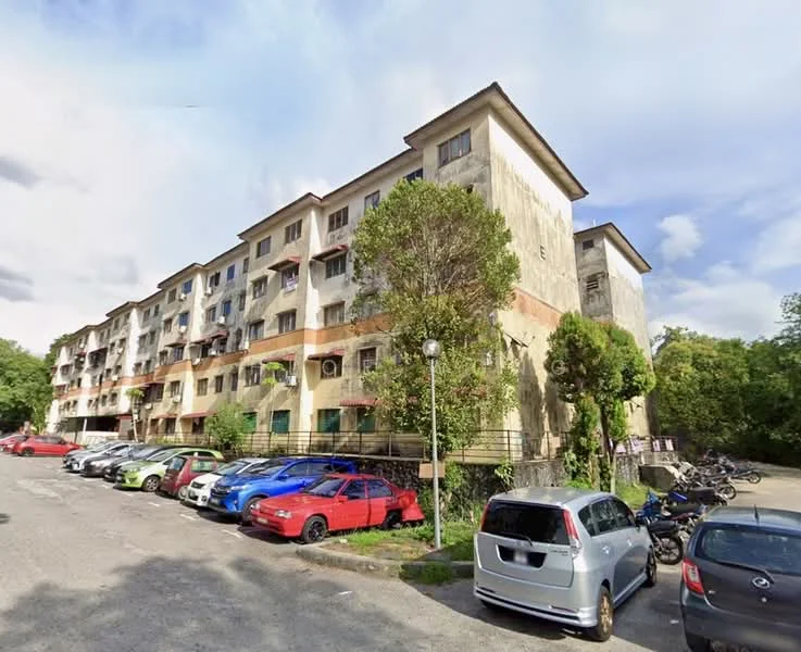 Exterior type: low-rise apartment block; features: weathered concrete facade, multiple balconies, visible air conditioning units, surrounding greenery, parking lot with multiple vehicles, two-storey building, mature trees nearby, open-air parking area; style: traditional.