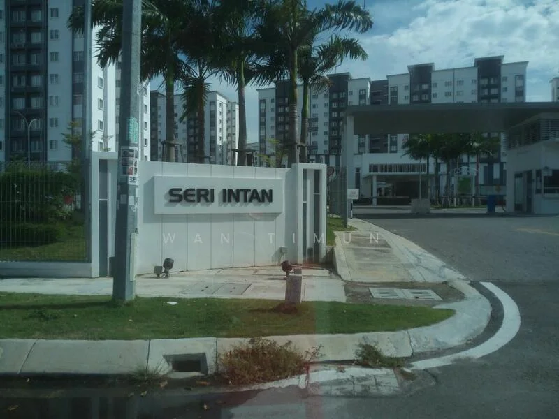 Exterior type: low-rise apartment block; features: white painted facade, manicured lawn, palm trees, paved walkway, entrance gate, signage with 'Seri Intan', surrounding greenery, parking area, multiple storeys visible; style: modern.