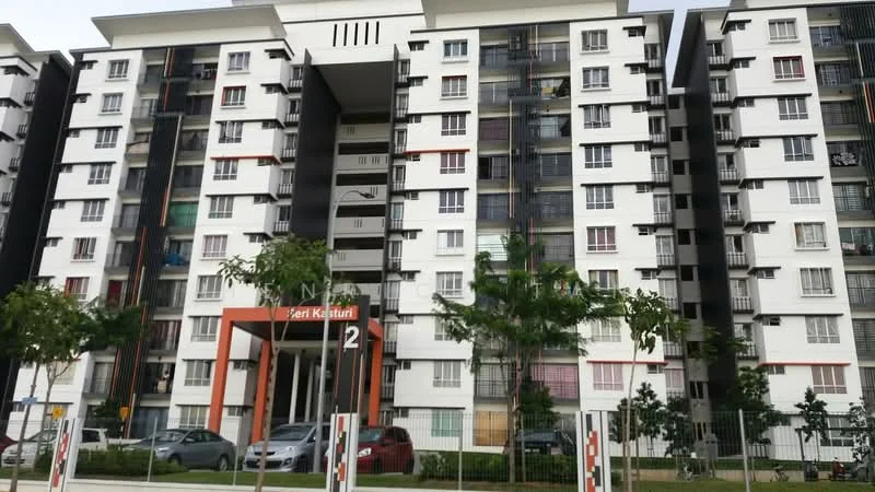 Exterior type: mid-rise condominium; features: white painted facade, red accent elements, balconies with railings, multiple windows, landscaped greenery in front, main entrance with signage, parking area visible, surrounded by paved walkway; style: modern.