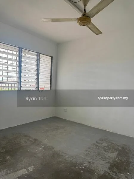 Room features: white painted walls, concrete flooring, 5-blade ceiling fan, large windows with metal grilles, natural light from windows.