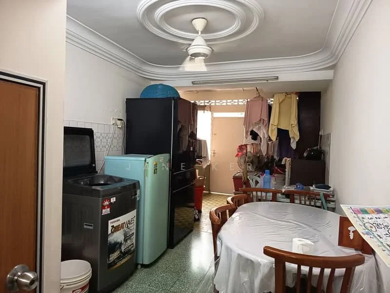 Kitchen features: green terrazzo flooring, white painted walls, tray ceiling with ceiling fan, double-door fridge in mint green, top-load washing machine, wooden dining table with four chairs, kitchen cabinets, window with natural light, clothes hanging on a rack, sink, countertop space.