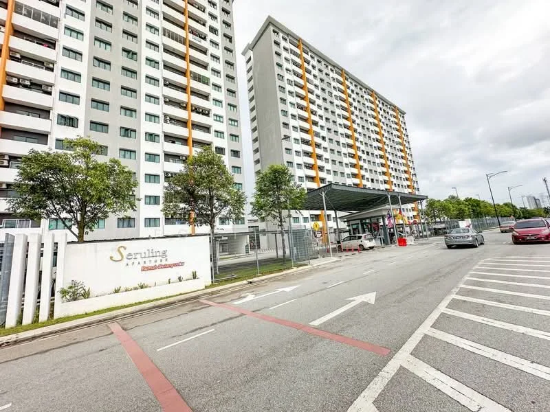 Exterior type: high-rise condominium; features: grey painted facade, orange accent panels, multiple storeys, main entrance with awning, landscaped entrance area, surrounded by trees, parking area visible, road access in front; style: modern.