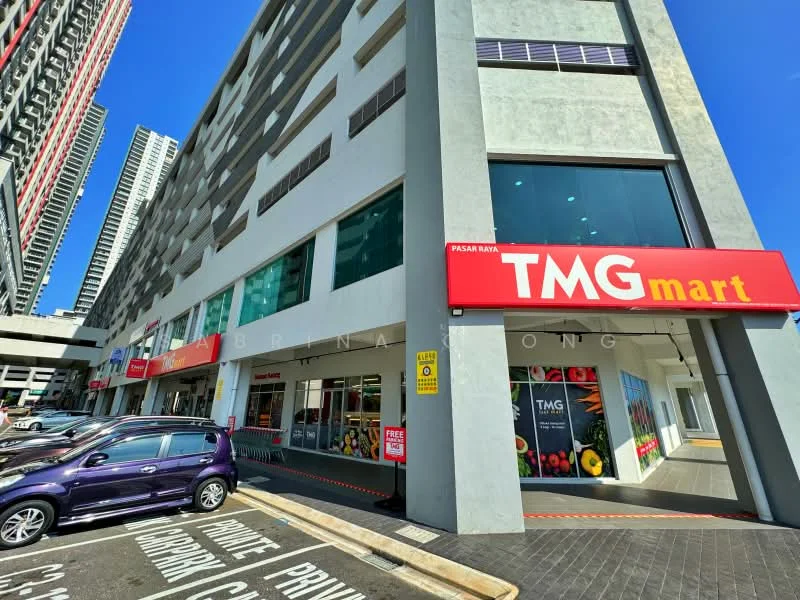 Exterior type: shophouse; features: glass facade, red signage with white text, multiple storefronts, parking lot in front, concrete exterior, large windows, awnings over entrances, surrounded by high-rise buildings; style: modern.