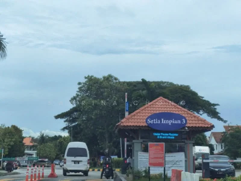 Exterior type: main entrance gate; features: entrance gate with tiled roof, signage for Setia Impian 3, surrounding greenery, paved road, traffic cones, vehicles in view, palm trees, cloudy sky; style: modern.