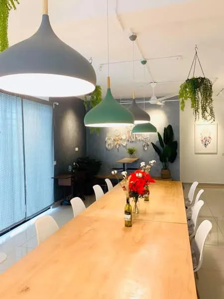 Dining features: long wooden dining table, white plastic dining chairs, green pendant lights, ceiling fan, grey accent wall, large windows with sheer curtains, decorative plants hanging from ceiling, vase with flowers on table; style: modern.
