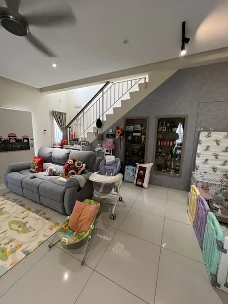 Living features: grey fabric sectional sofa, decorative throw pillows, area rug with colorful pattern, white tiled flooring, ceiling fan, wall-mounted mirror, staircase with metal railing, wall with grey accent, decorative shelving unit, baby stroller, playpen, baby bouncer, wall-mounted light fixtures; style: modern.
