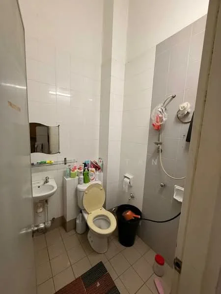 Bathroom features: white tiled walls, grey tiled wall section, ceramic tile flooring, one-piece toilet, sink with chrome faucet, mirror above sink, shower area with handheld shower, waste bin, various toiletries on sink, shower caddy, bath mat.