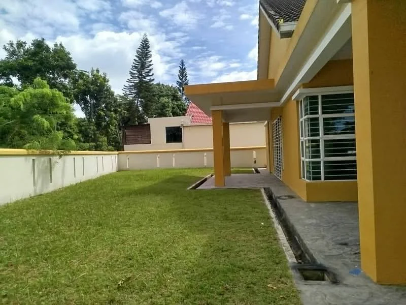 Exterior type: detached bungalow; features: yellow painted facade, flat roof, manicured lawn, surrounded by greenery, concrete walkway, large windows, outdoor patio area, single-storey, garden area; style: modern.