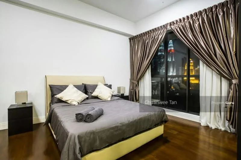 Bedroom features: king-size bed with upholstered headboard, grey bedding with decorative pillows, nightstand with lamp, floor-to-ceiling windows, brown curtains, wooden flooring, city skyline view, decorative towels rolled on the bed; style: modern; view: city.