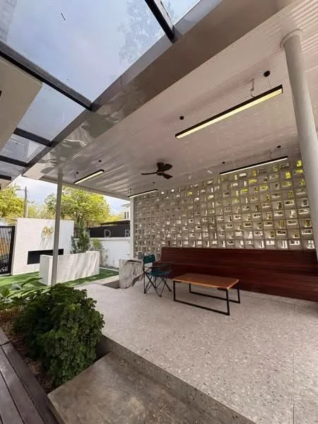 Exterior features: covered patio area, exposed ceiling with lighting, ceiling fan, decorative wall with cut-out patterns, wooden bench seating, concrete table, landscaped garden area, green lawn, stone feature wall with water feature, paved flooring; style: modern.