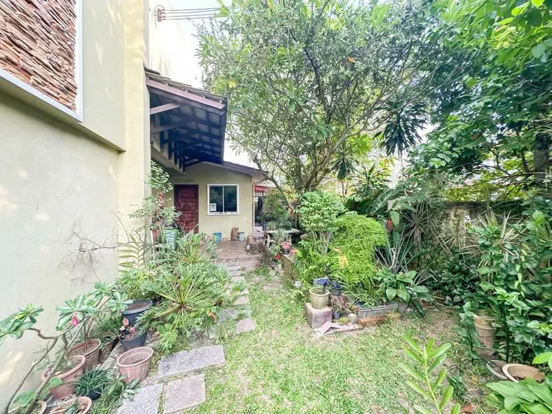 Exterior type: detached bungalow; features: manicured lawn, mature trees, stone-paved walkway, various potted plants, greenery surrounding the entrance, wooden door, overhanging roof, exterior wall with light yellow paint; style: traditional.
