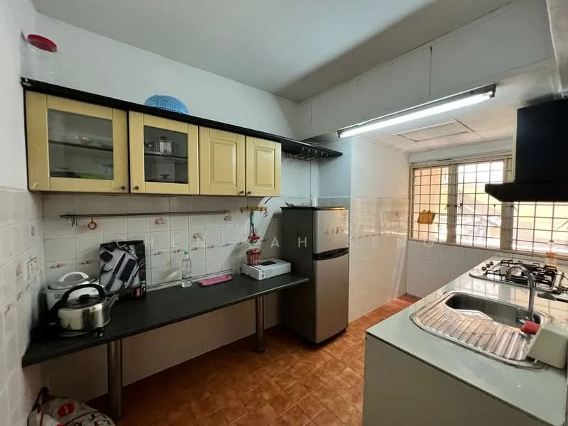 Kitchen features: yellow cabinetry with glass-front upper cabinets, black countertop, stainless-steel sink, chrome pull-down faucet, built-in gas hob, stainless-steel range hood, stainless-steel fridge, white tiled walls, orange ceramic tile flooring, window with metal grille, overhead fluorescent lighting, kitchen appliances including kettle, water dispenser.